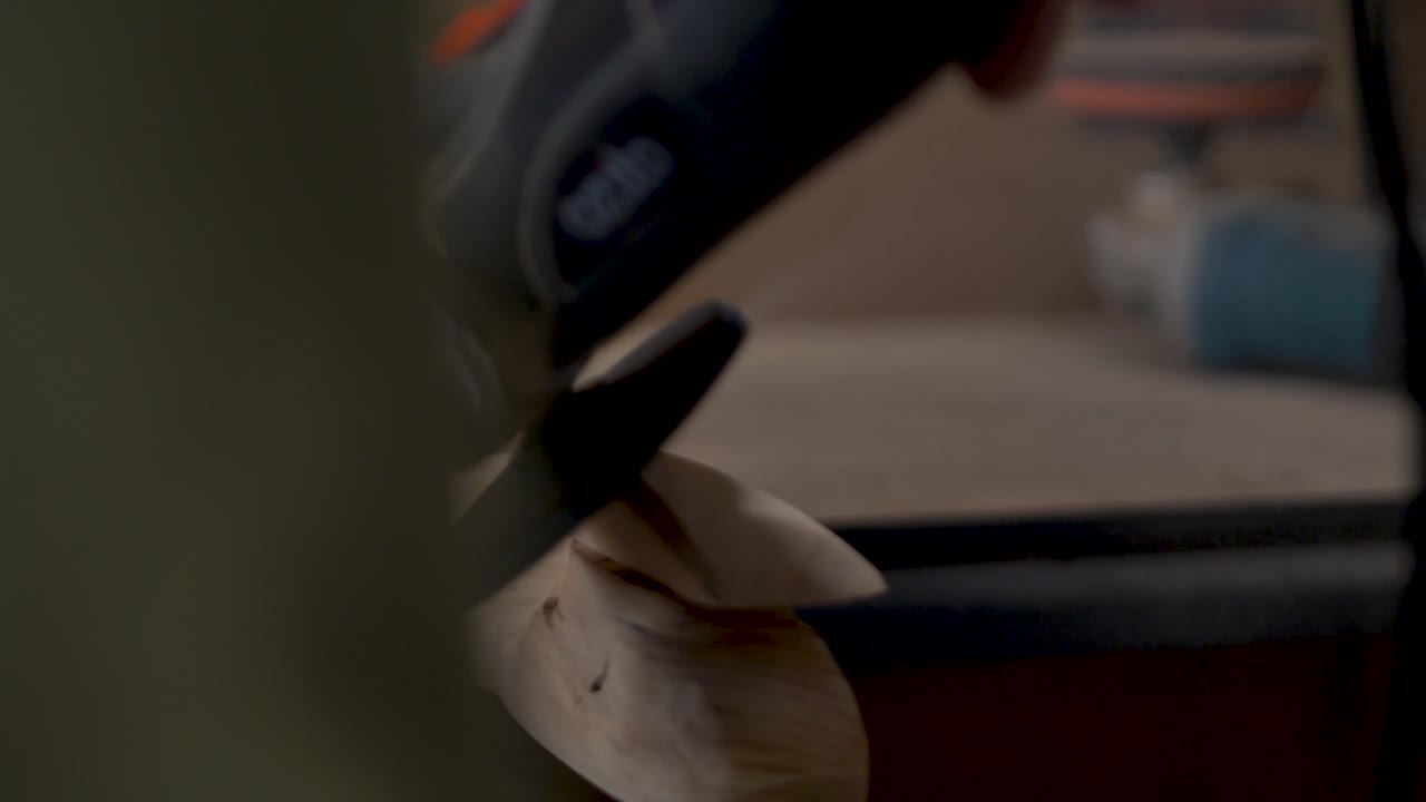 Slow motion close-up of man using electric grinder machinery power tool to shape wooden hardwood blocks for indoor climbing holds on woodwork bench at home garage shed in Australia carpentry project