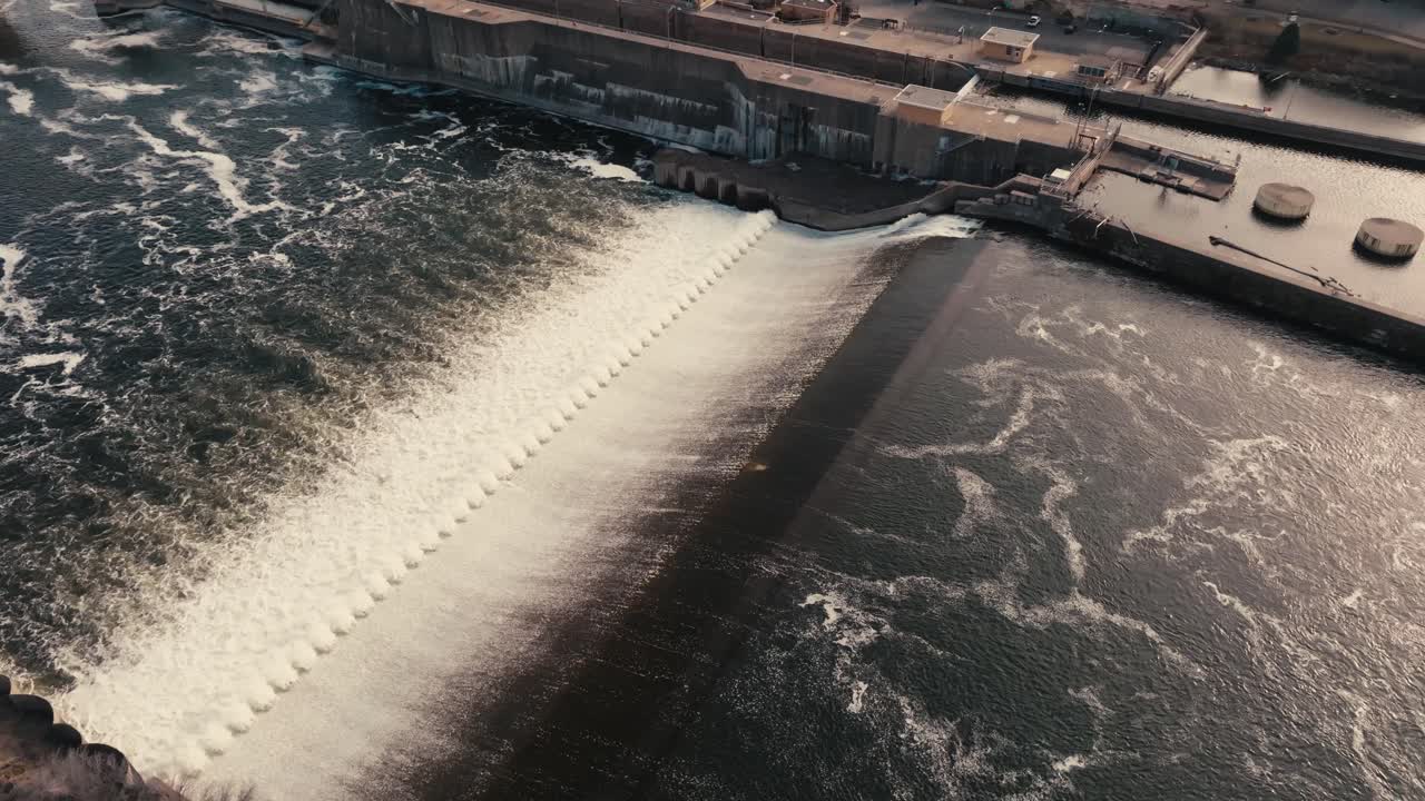 aerial drone shot of a river flowing over a lock and dam in a downtown city during golden hour