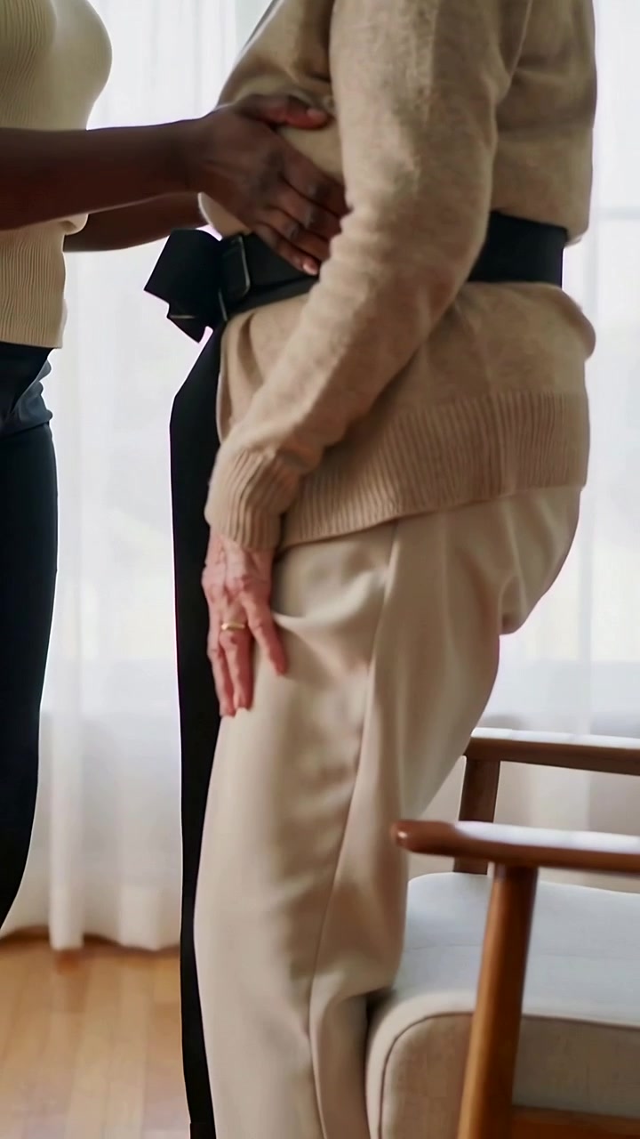 Vertical video: Placing belt caregiver supporting Senior rising from chair, standing safely at home