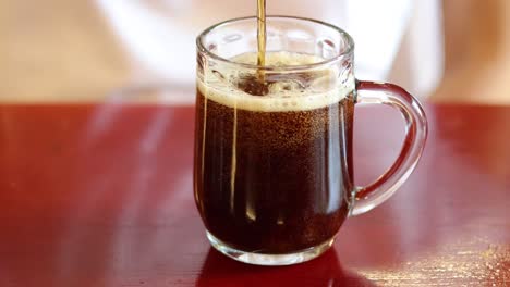 pouring a bubbly dark beverage into a clear mug