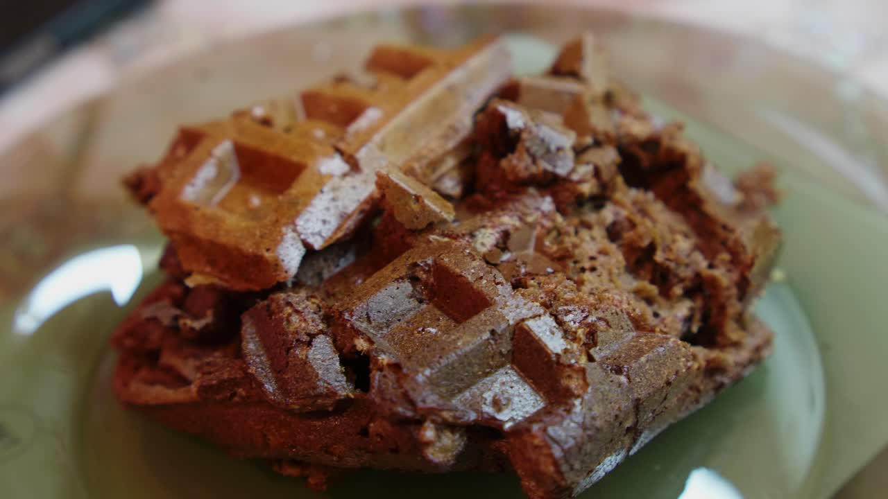 A plate holds a poorly made waffle. The scene takes place at a kitchen table during breakfast. The lighting shows a typical morning setup with simple decor