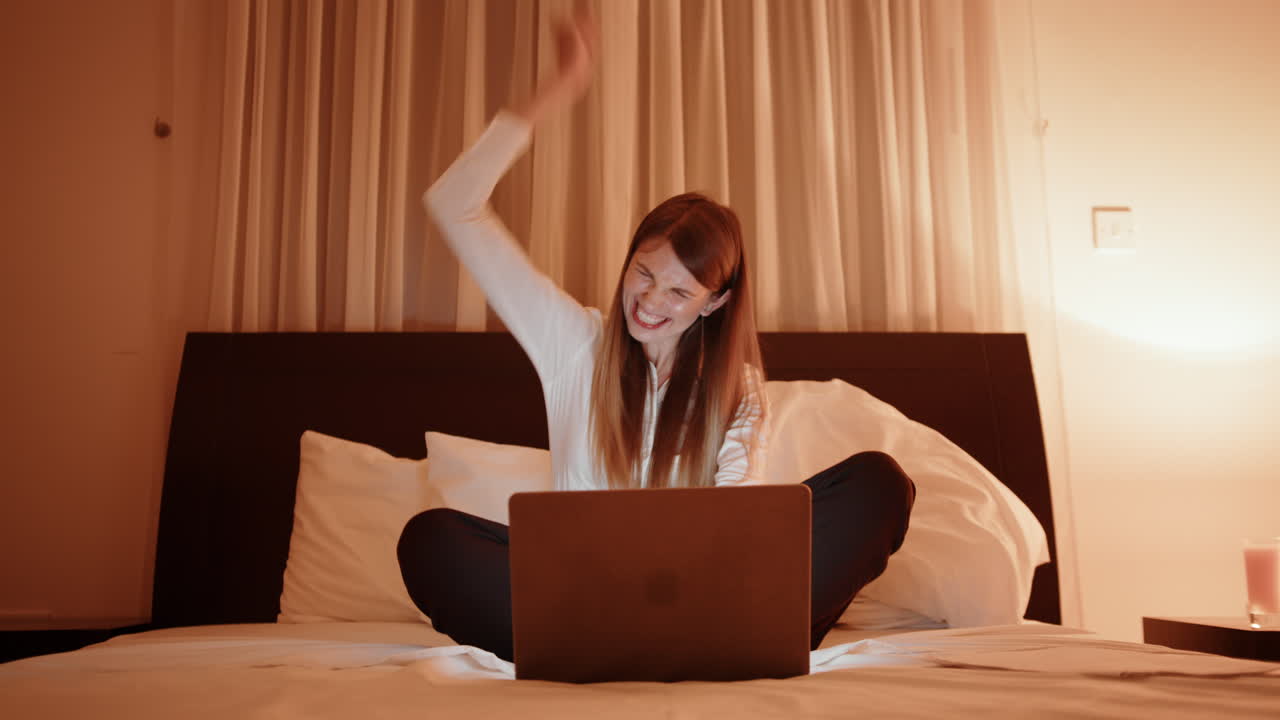 밤에 침대에서 노트북에서 성공을 축하하는 여자