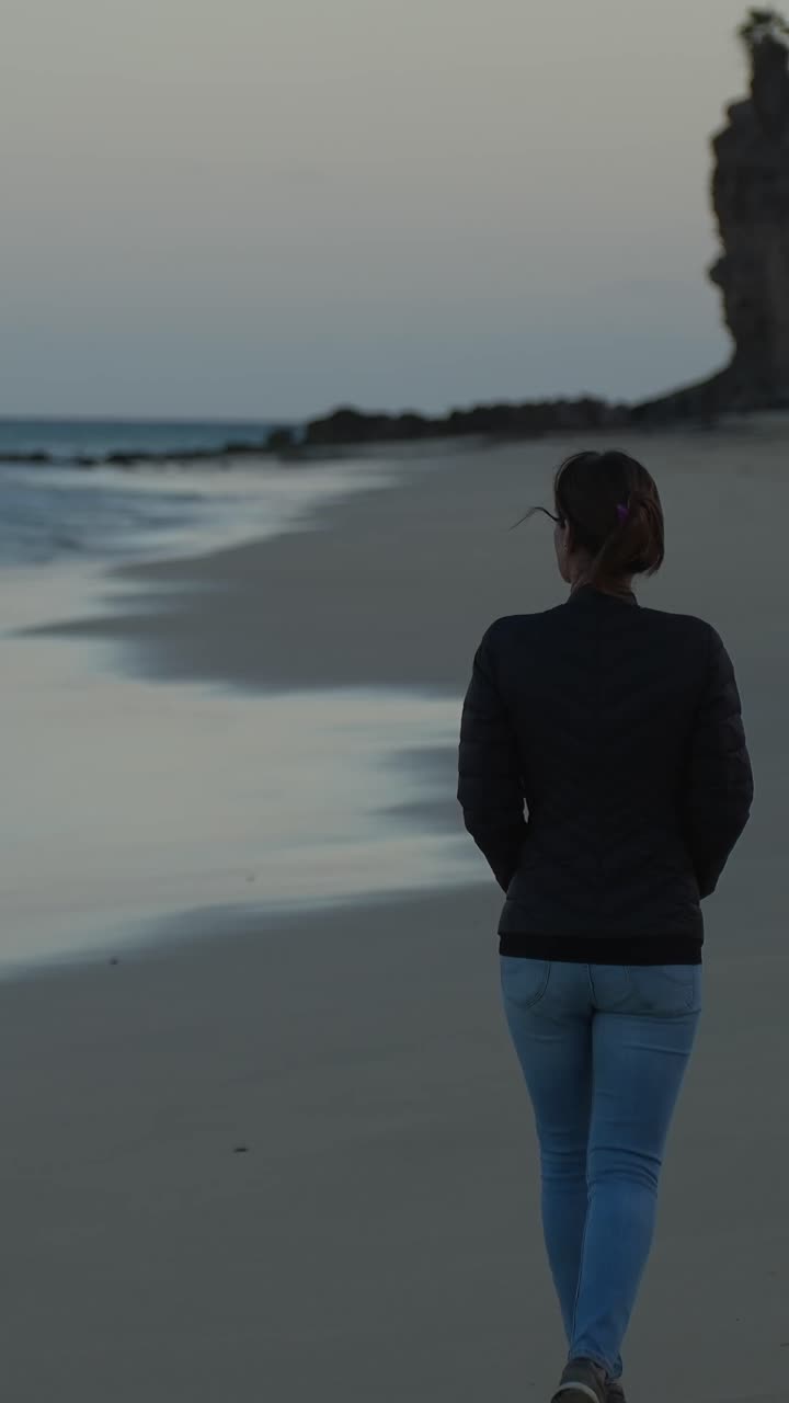 Donna sola che cammina su una spiaggia sabbiosa al crepuscolo, godendosi l'oceano calmo e la solitudine