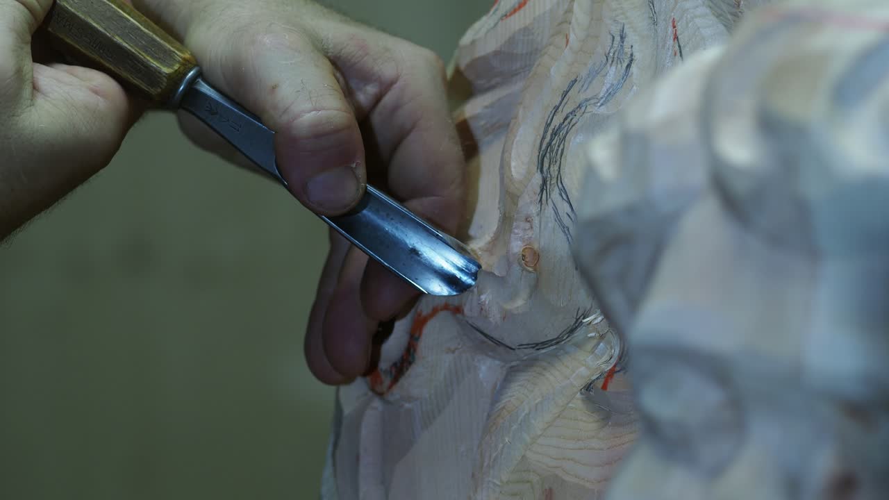 Close up of skilled hands meticulously carving intricate details into a sculpture using a sharp chiseling tool with focus on the woodworking process