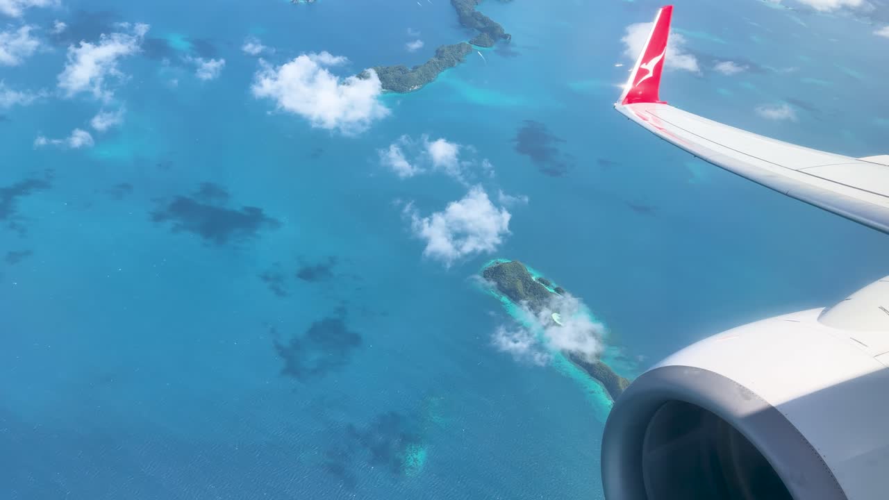 Luftperspektiv fra et passagerfly, der flyver over tropiske turkise farvande og frodige grønne øer.