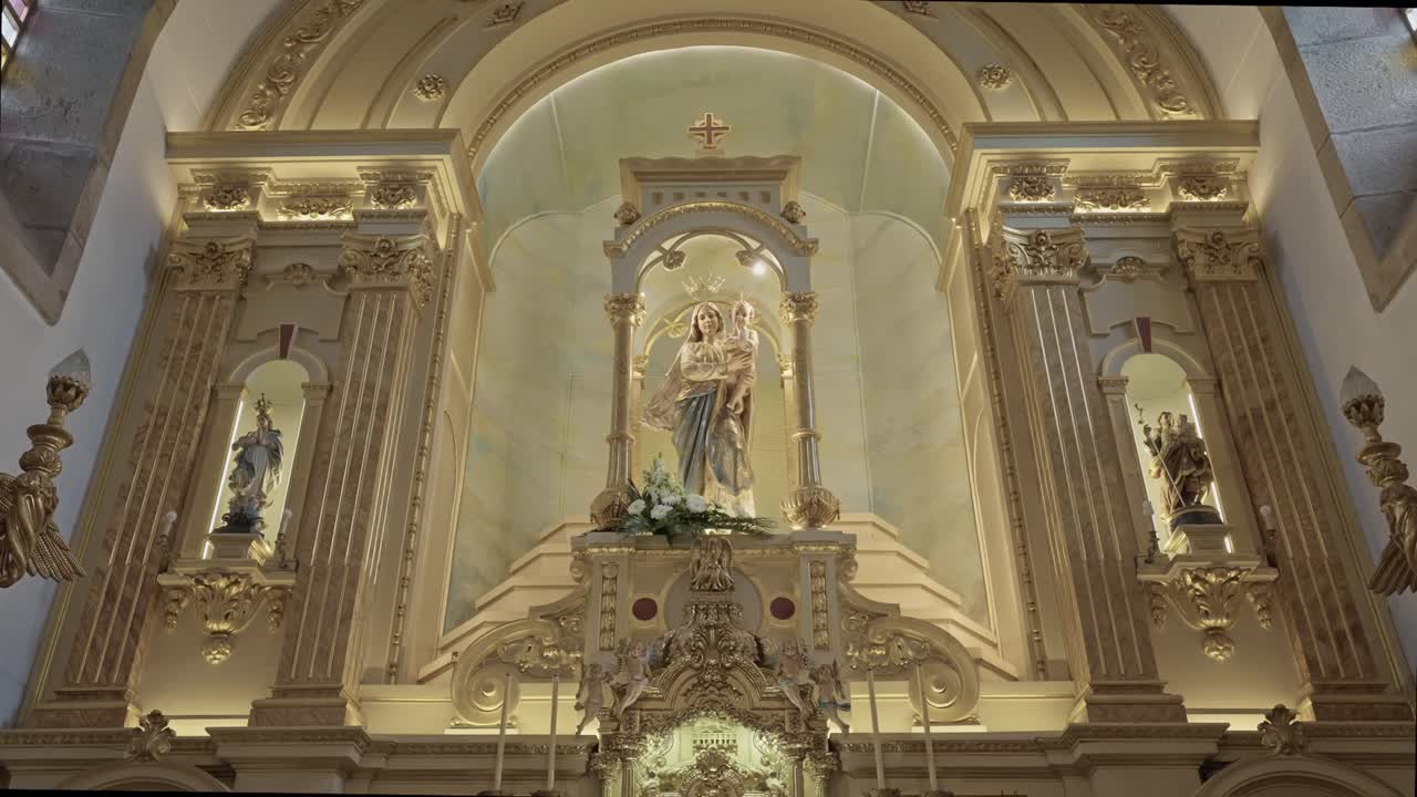 Interiér katolického kostela s bohatě zdobeným oltářem se sochou Panny Marie umístěnou uprostřed mezi sloupy, oblouky a posvátnými architektonickými detaily.