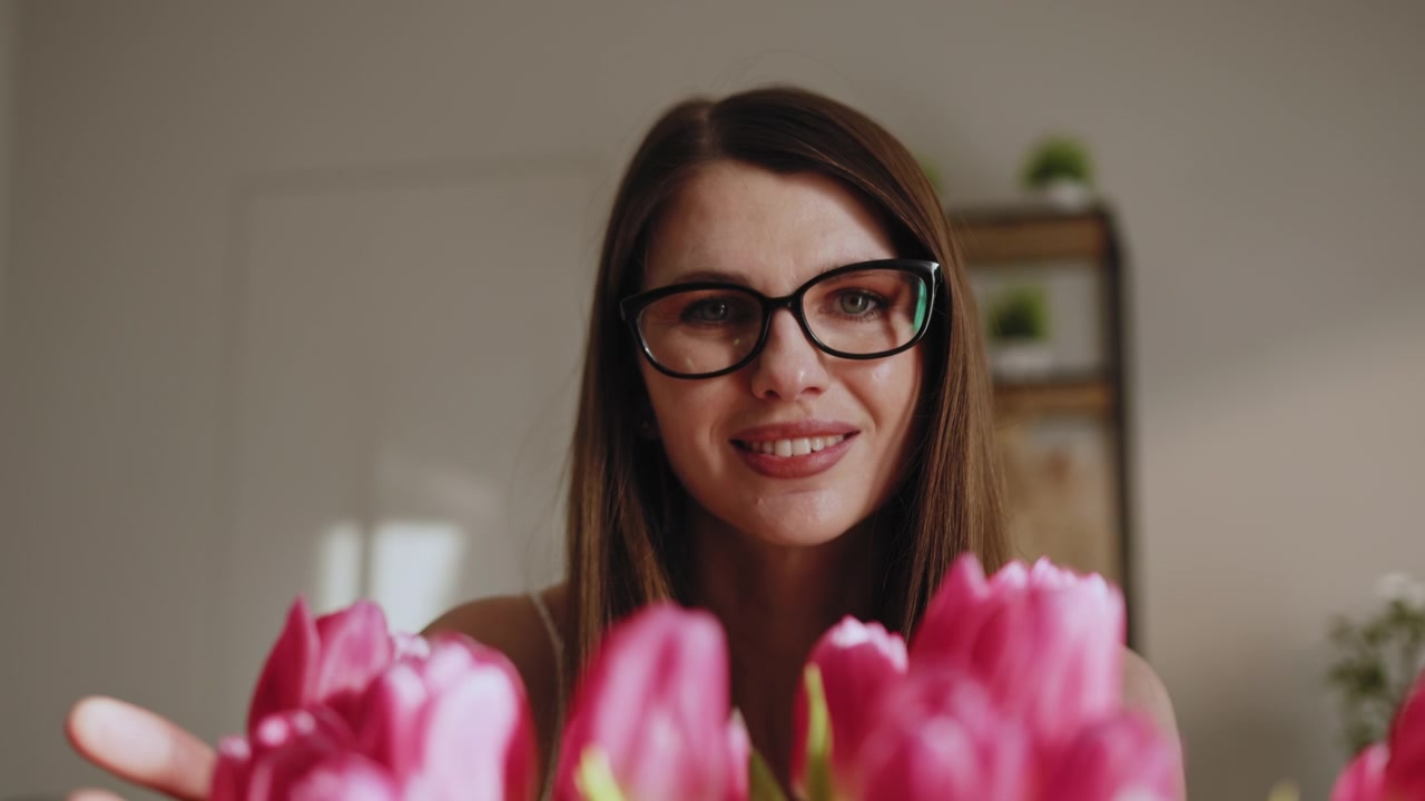 Giovane donna con gli occhiali tocca delicatamente vivaci tulipani rosa mentre sistema un bellissimo bouquet in casa