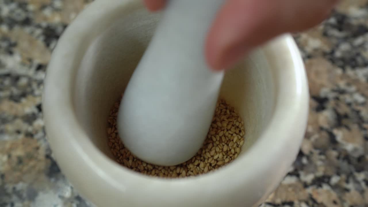 Grinding toasted sesame seeds in a marble pestle and mortar. Close up.