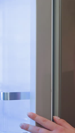 vista de la mano de la dama en vestido rosa abriendo suavemente la puerta del refrigerador, una suave luz azul ilumina el interior mientras se mueve hacia adelante para inspeccionarlo, mientras que el fondo permanece ligeramente borroso