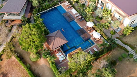 hotel in asia with palms and swimming blue pool and young boy is swimming during sunset dronevideo