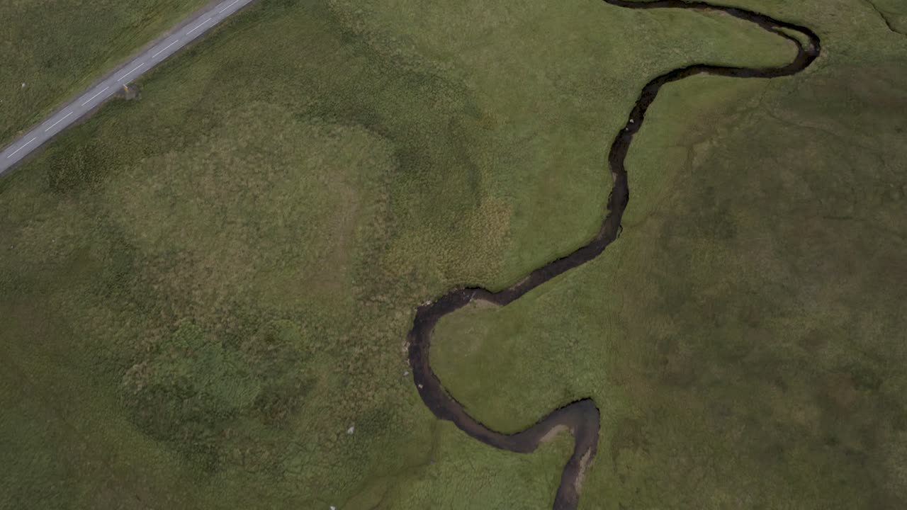Aerial view of a small meandering stream winding through a lush green valley with moss and grass in the Icelandic highlands