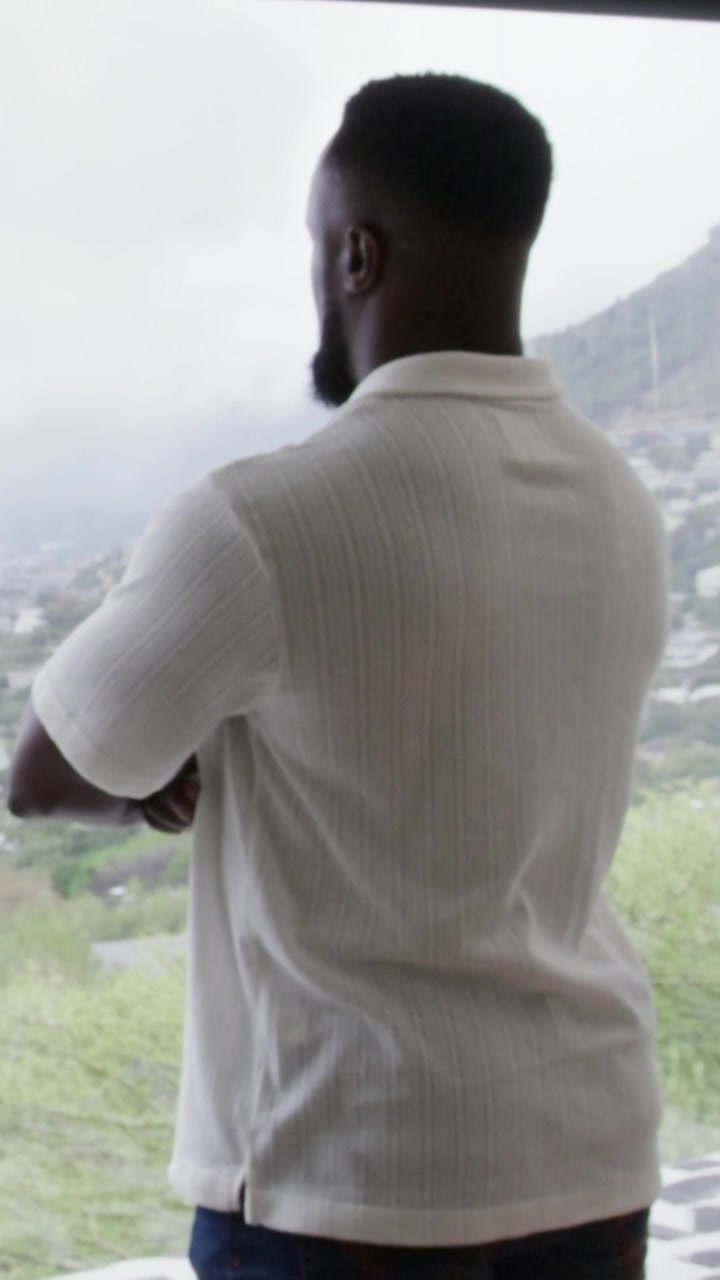 Vertical video: Sequence starting with man in white shirt standing at room window, observing valley