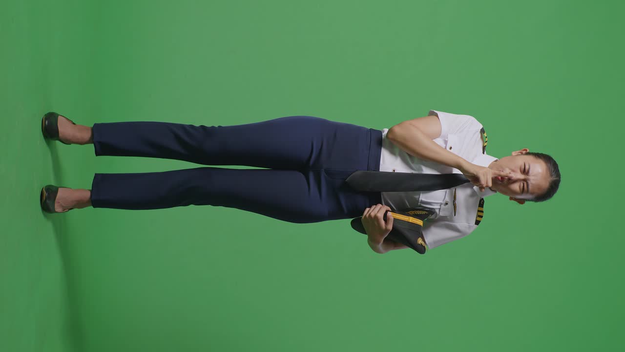 아시아 여성 조종사가 카메라를 바라보고 녹색 스크린 배경 스튜디오에서 shh 제스처를합니다.