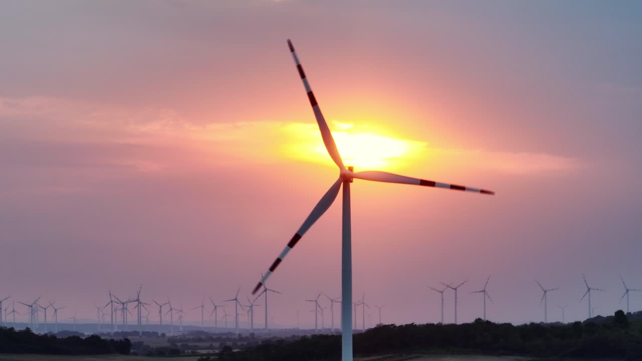 풍력 터빈이 우아하게 회전하면서 태양이 그 뒤에 서서 재생 가능한 에너지와 자연 사이의 조화를 상징합니다.