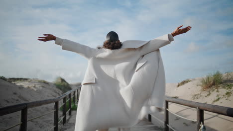 girl spread arms open at windy beach rear view. relaxed woman enjoying moment