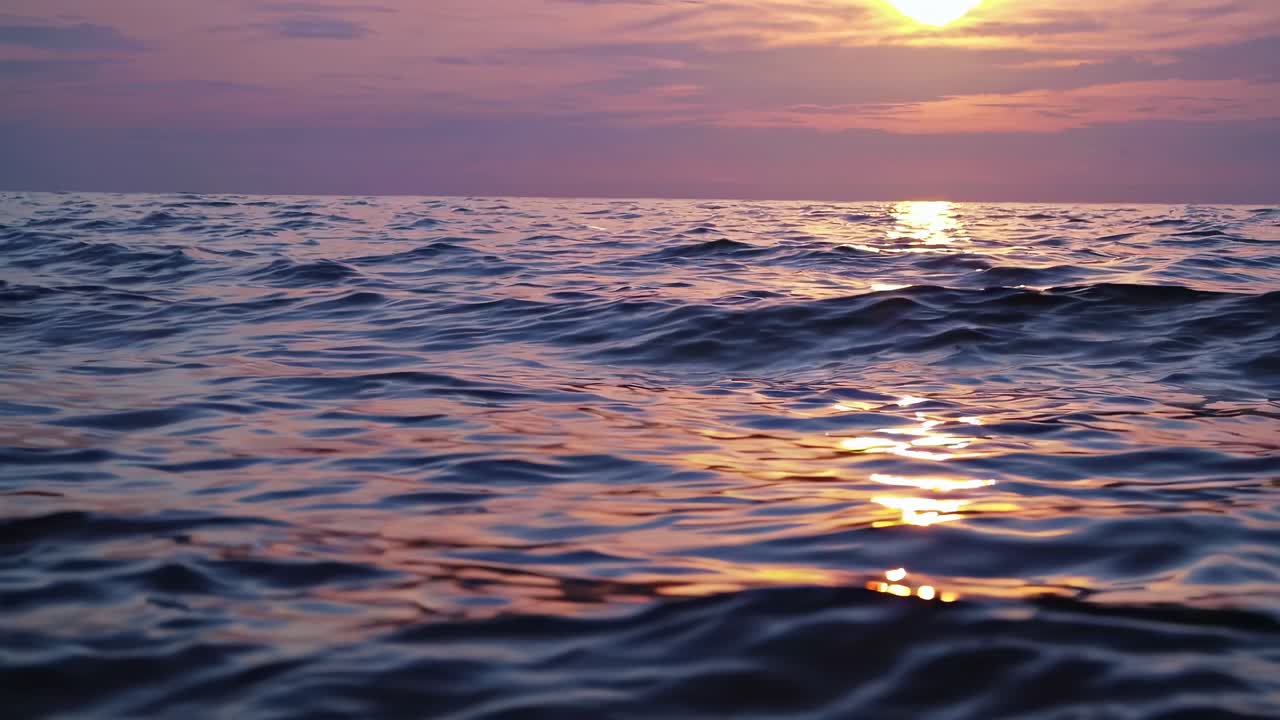 A serene ocean sunset video with gentle waves. Captured from a low angle, highlighting the water's