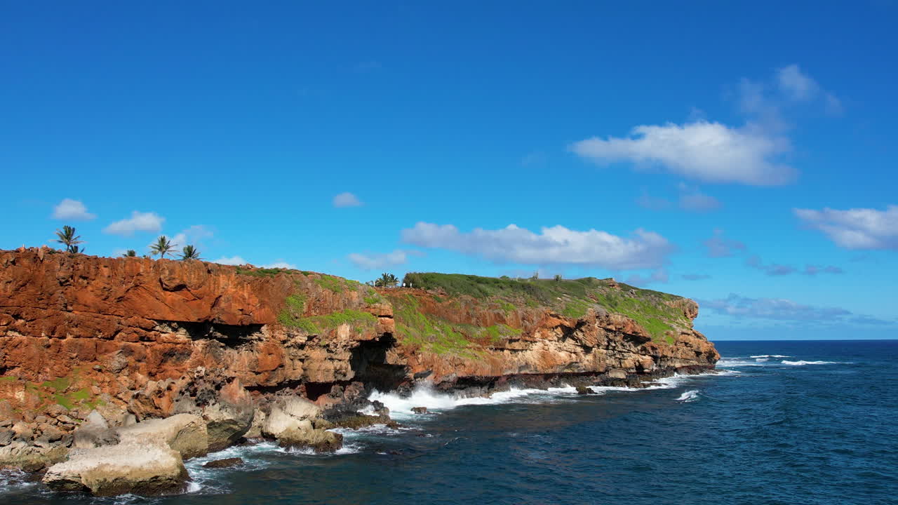 A low angle drone shot from the ocean approaching a Hawaiian cliffside.