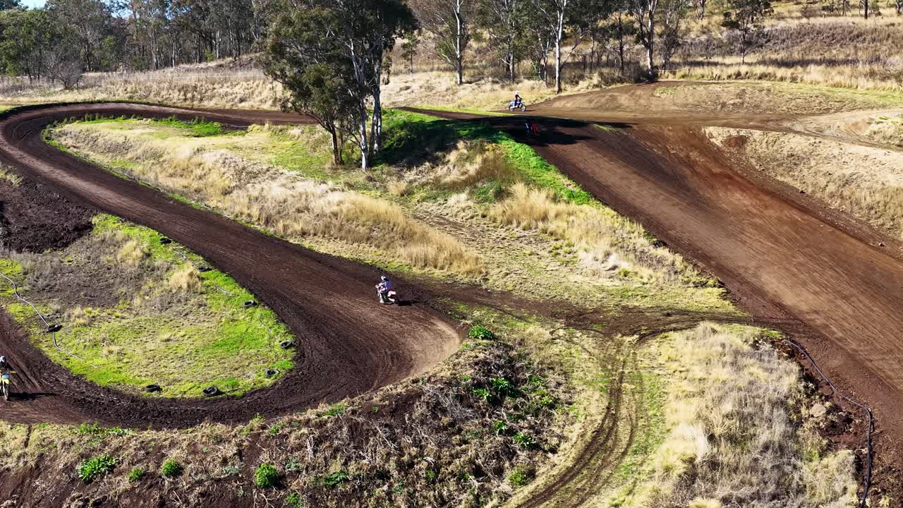 Motocross rider speeds through winding dirt track, aerial view, bright daylight, rural Australian landscape