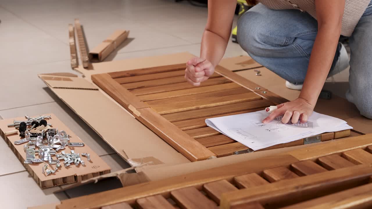 A person assembles wooden furniture using screws and bolts, following instructions in a well-lit indoor setting