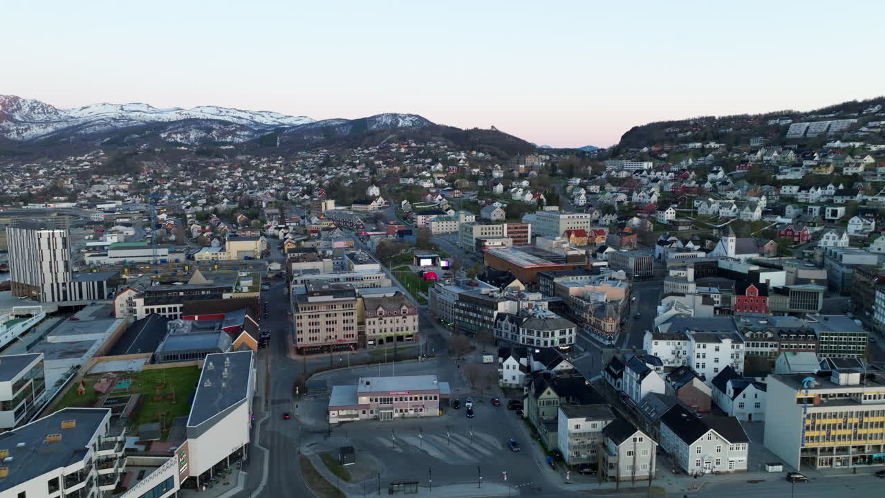 Aerial view of Harstad, Norway, showing coastal neighborhoods, winter mountains and the city center during calm evening light, highlighting the scenic Arctic urban landscape