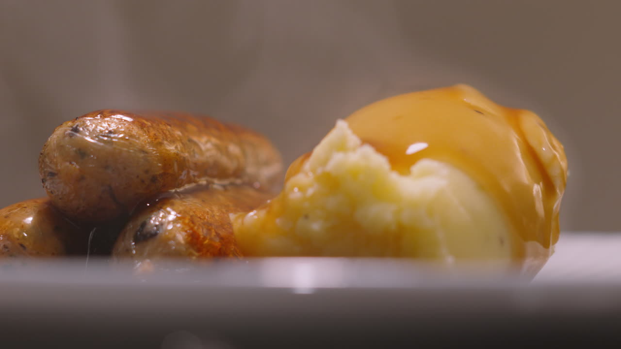 Sugo versato su un delizioso piatto fumante di cibo tradizionale, con salsicce vegane grigliate dorate servite su purè di patate. Perfetto per food blog e promozioni di ristoranti