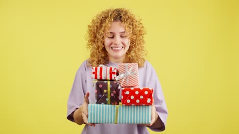 woman with curly hair holding a stack of colorful gifts on yellow background