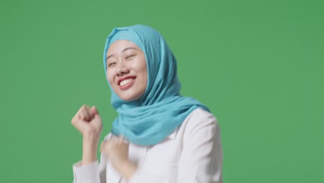 녹색 스크린 배경 스튜디오에 서서 미소 짓고 춤을 추는 아시아 무슬림 여성의 클로즈업