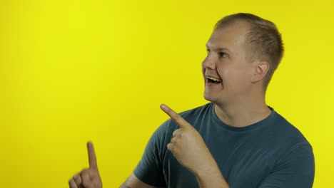 Portrait-of-young-man-posing-in-green-t-shirt.-Happy-smiling-guy-pointing-at-something-with-hand