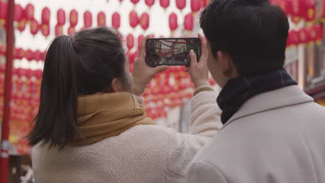 pareja asiática de vacaciones tomando fotos en chinatown en londres, reino unido en el teléfono móvil