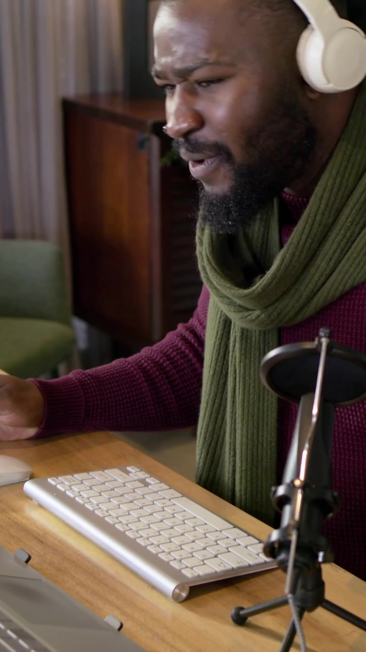 Vertical video: Starting man with scarf podcasting with mic, gesturing and typing at home desk keys