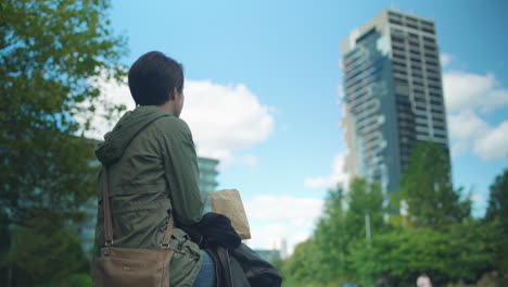 woman with short hair looking around park with large condo building nearby