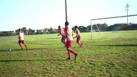 playing soccer on field, male players in red uniforms running towards goal