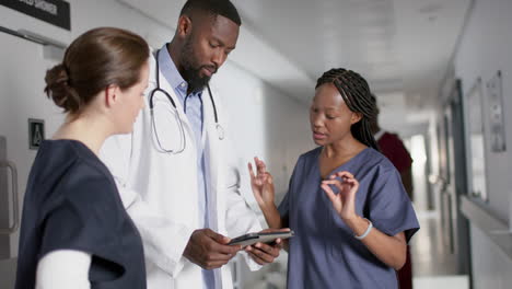 diverse male and female doctors discussing work, using tablet in corridor at hospital, slow motion
