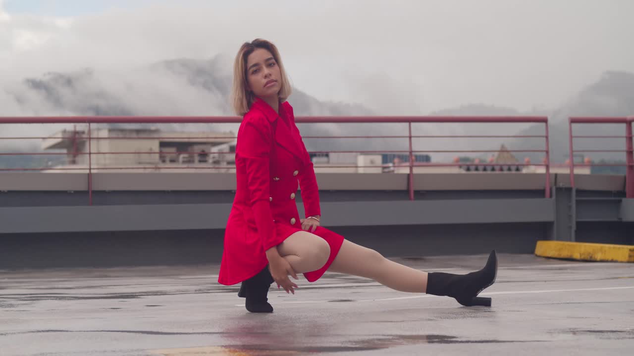 en el tejado urbano, una joven hispana se para con gracia en su corto traje carmesí