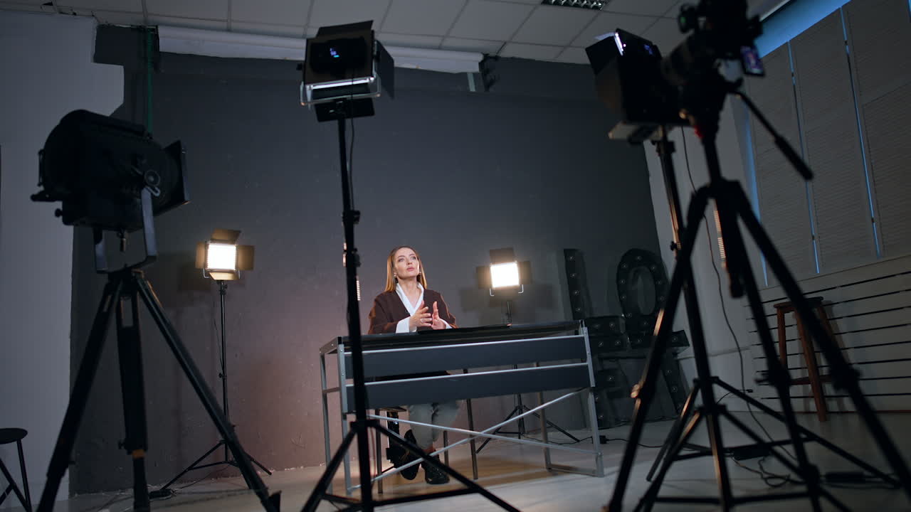 Caucasian woman sitting at desk speaking and gesturing while recording a video. Studio footage of blog content. Low angle view.