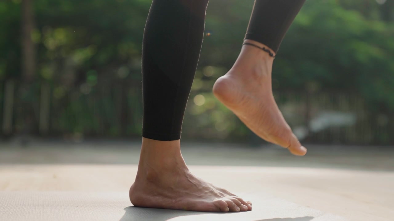 Barefoot woman in yoga pose outside, captured in slow motion on a sunny day