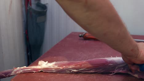 the butcher's hands cut fat pieces of pork tenderloin with a knife