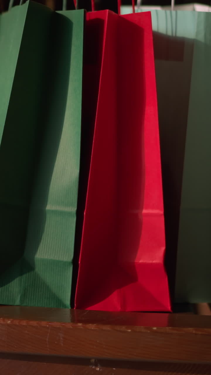tres bolsas de compras en colores rojo, verde y verde menta son colocadas en un banco de madera marrón por una dama con un vestido rosa, se sienta con las piernas cruzadas, relajándose después de comprar