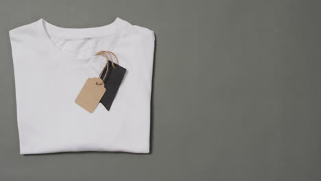 Video-of-flat-lay-of-white-t-shirt-with-tags-and-copy-space-on-grey-background