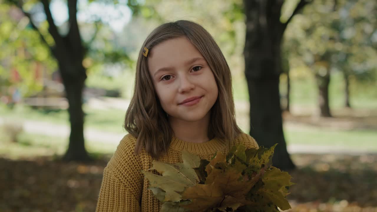 Portrait of smiling little girl with bouquet of autumn's leaves.