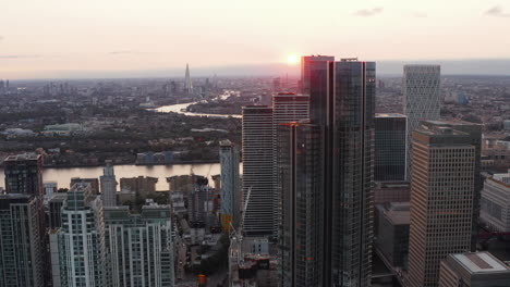 Forwards-fly-around-group-of-tall-skyscrapers-in-Canary-Wharf-business-centre.-Aerial-panoramic-view-of-city-in-sunset-time.-London,-UK