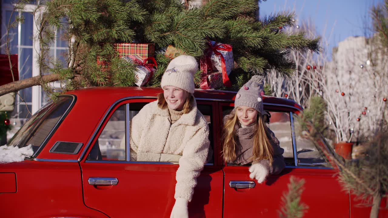 niñas adolescentes riendo mirando por la ventana del coche con árbol de navidad decorativo en el techo. chicas jóvenes felices en el coche rojo con árbol de año nuevo y regalos. expresión de emoción positiva en la víspera de navidad.