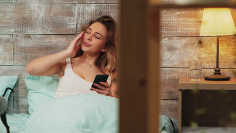 Ampliar-La-Foto-De-Una-Mujer-Cansada-En-Pijama-Usando-Su-Teléfono-Inteligente