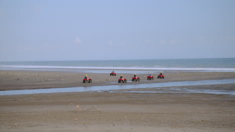 A-group-of-ATV-Quad-bikes-riders-driving-along-the-beach-during-a-tourist-adventure-tour-in-Bali,-Indonesia