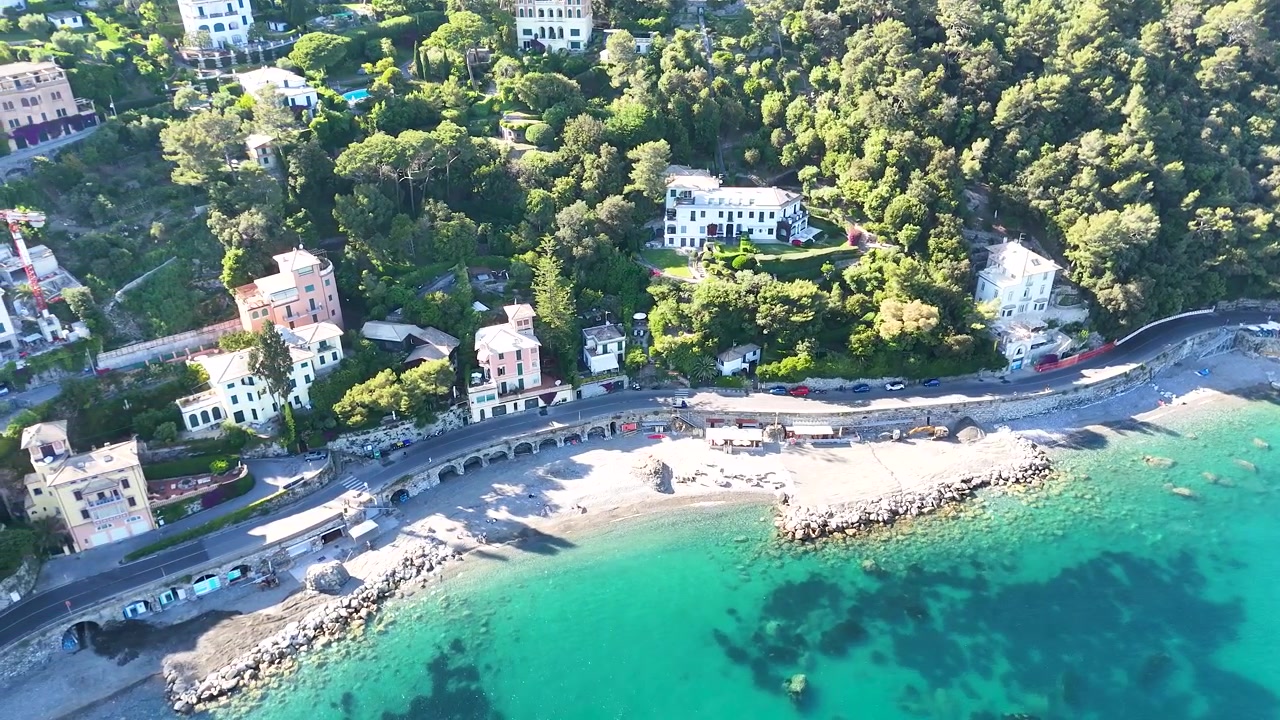 Vista aerea con drone di ville colorate lungo il Mar Mediterraneo turchese sotto un sole splendente.