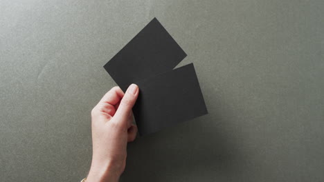 mano de mujer caucásica sosteniendo dos tarjetas de visita negras en fondo gris, espacio de copia, cámara lenta