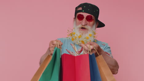 hombre de edad avanzada muestra bolsas de compras anunciando descuentos, asombrado con los precios bajos en los días festivos del viernes negro