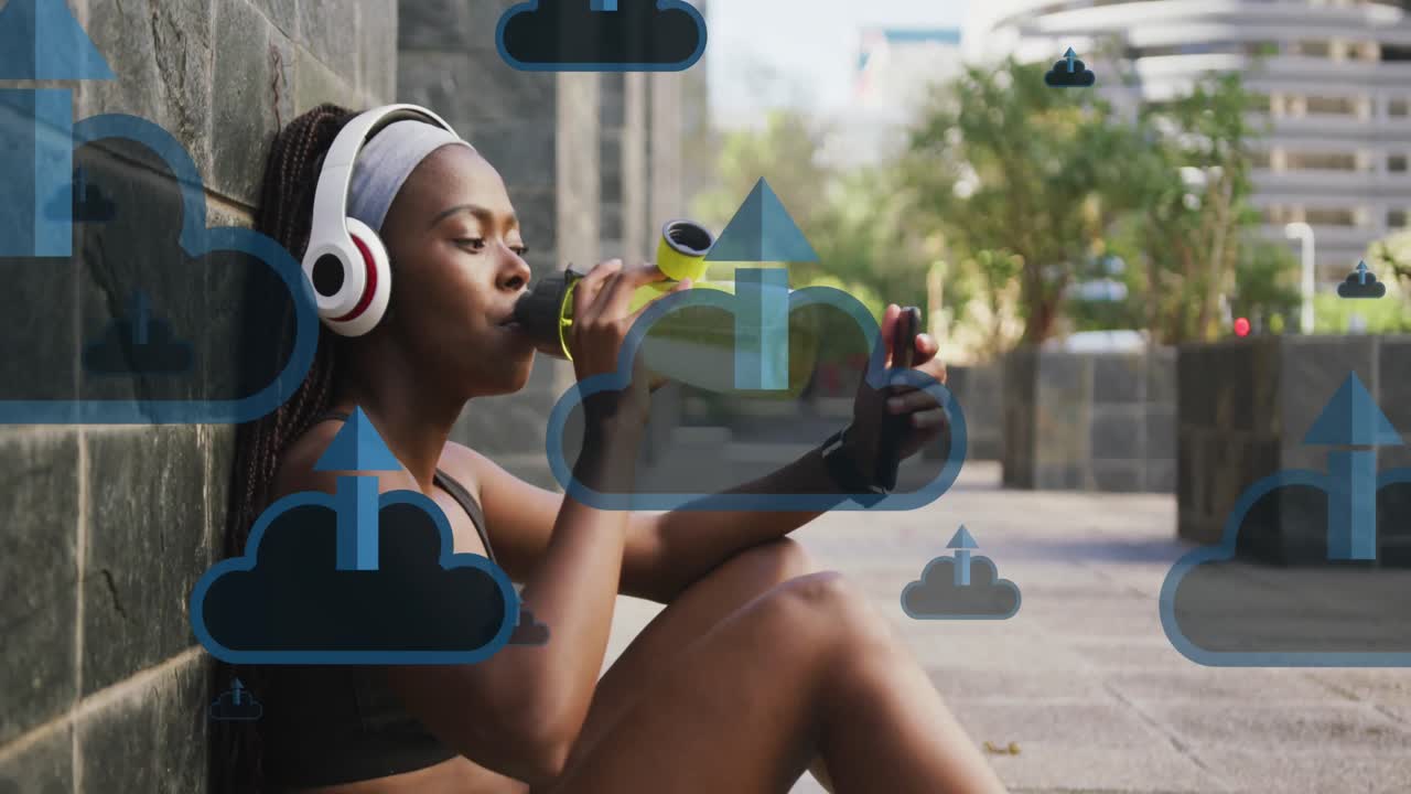 Animation of cloud, arrow icons, african american woman watching video over phone and drinking water