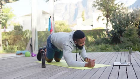 Hombre-Afroamericano-Enfocado-En-Entrenamiento-Físico-Haciendo-Ejercicio-En-Cubierta-En-Un-Jardín-Soleado,-Cámara-Lenta