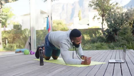 focused african american man fitness training exercising on deck in sunny garden, slow motion